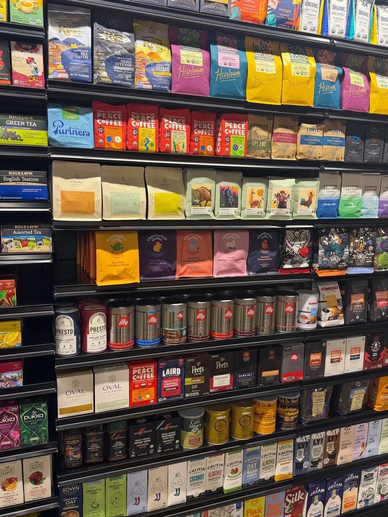 Oval Coffee Roasters whole-bean bags on an upper shelf and single-serve pour-over boxes below at Atherea Natural Market near Union Square, New York City; yellow, green and orange labels distinguish the coffee profiles.