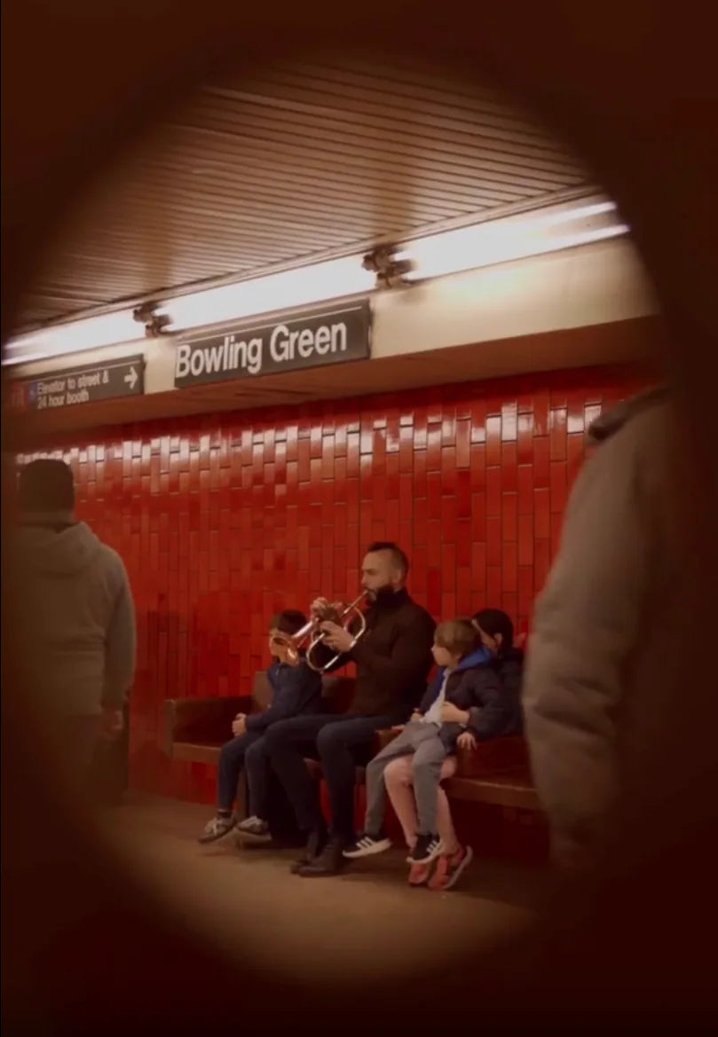 Dr. Jonathan Saraga playing music beside the red tiled walls of Bowling Green station.