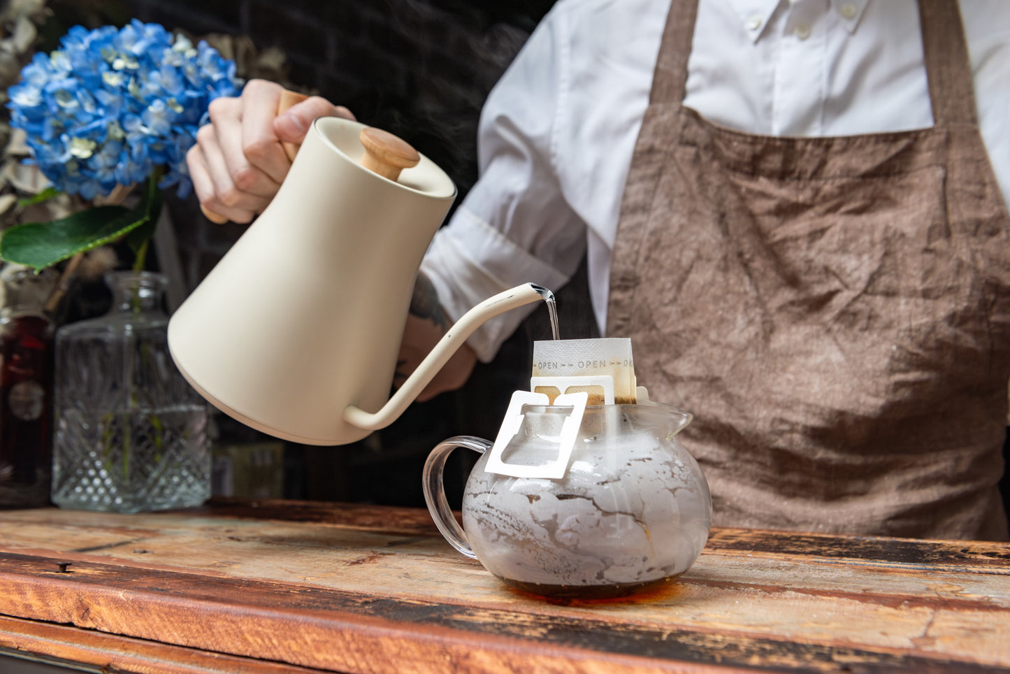 Christopher Alspach, co-founder of Oval Coffee Roasters, pouring hot water over a single-serve pour-over drip bag, showcasing NYC-roasted light roast coffee.