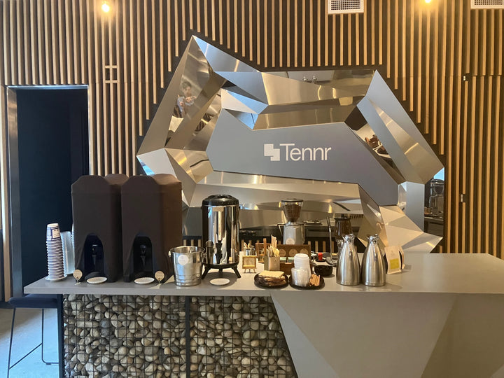 Oval Coffee Roasters resident hospitality catering setup in downtown New York City, with coffee dispensers, a stainless-steel urn, grinder, thermal carafes and cups beneath Tennr signage.