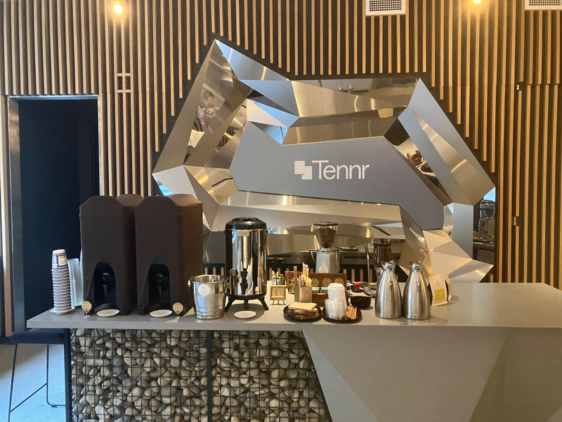 Oval Coffee Roasters resident hospitality catering setup in downtown New York City, with coffee dispensers, a stainless-steel urn, grinder, thermal carafes and cups beneath Tennr signage.