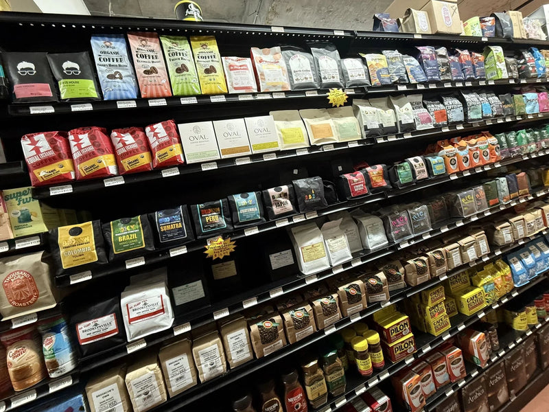 Oval Coffee Roasters whole-bean coffee bags and single-serve pour-over boxes on a black coffee shelf at Beyond Natural Market in Williamsburg, Brooklyn, with yellow, orange and green labels identifying the three profiles.