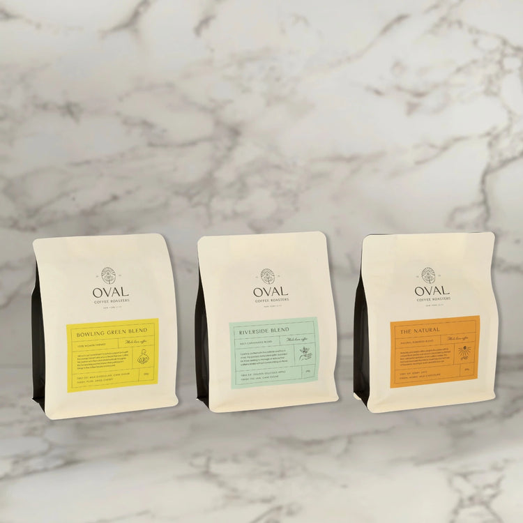 Oval Coffee Roasters Whole Bean Variety Pack featuring Bowling Green Women-Grown light roast coffee, Riverside Half Caff coffee, and The Natural natural process light-to-medium roast coffee, photographed together as a specialty coffee gift set for home brewing, office coffee, and holiday gifting.