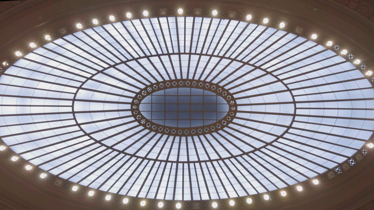 Upward view of an oval skylight at the National Museum of the American Indian in New York City, with radiating glass panels, dark framing and a ring of lights.