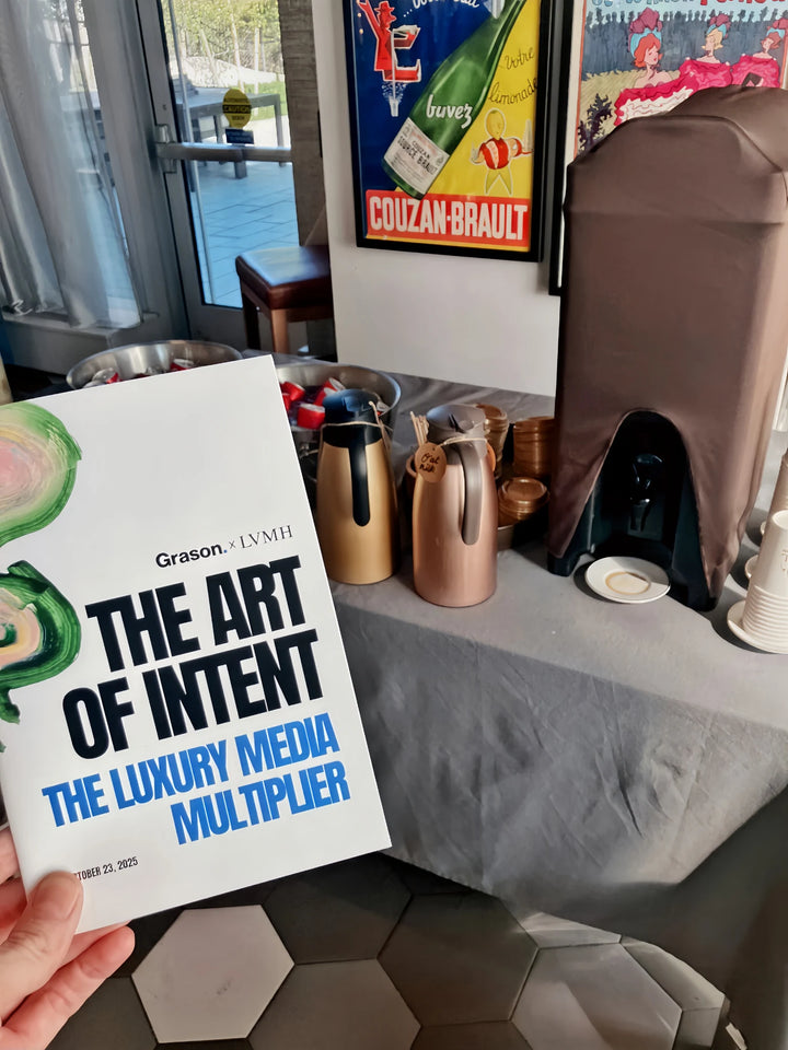 An event booklet titled The Art of Intent held beside Oval Coffee Roasters catering at an LVMH event at One Manhattan Square, with gold carafes, stacked cups and a covered coffee urn.