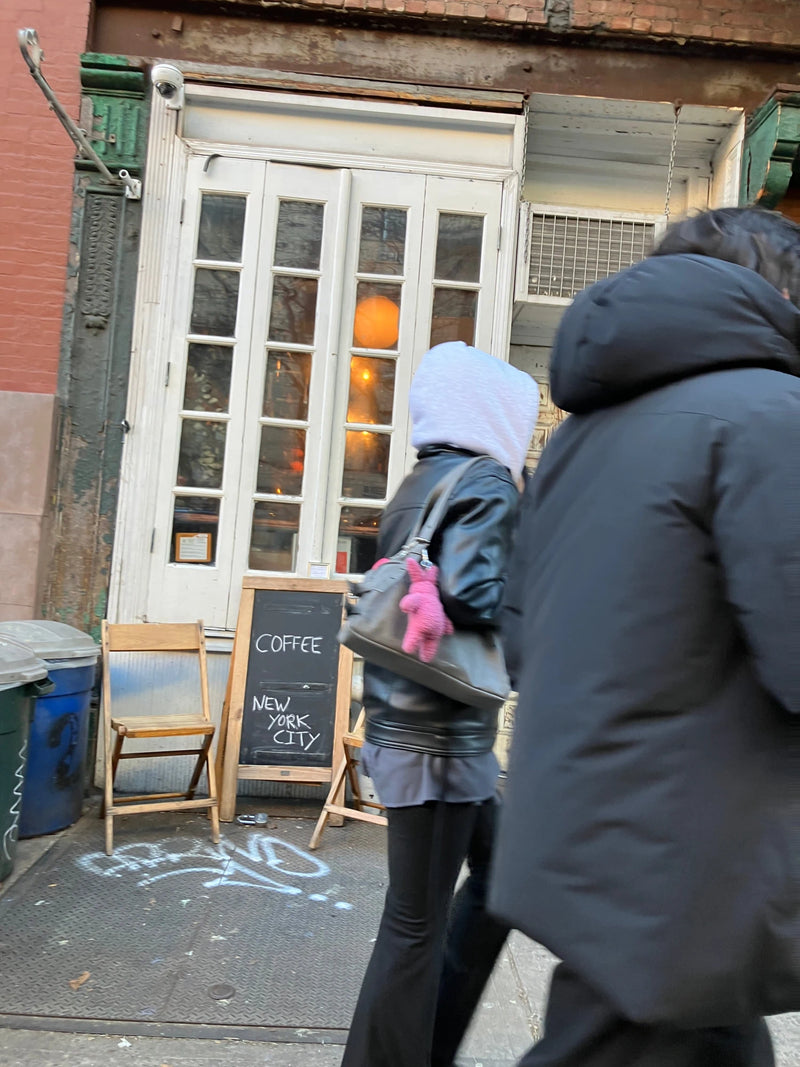 Guests in winter coats outside an Oval Coffee Roasters pop-up in New York City’s East Village, passing white windowed doors, wooden folding chairs and a chalkboard reading Coffee New York City.